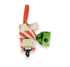 Orange and white striped fabric pet waste bag dispenser with an orange carrying loop and black clip, holding a green paw-print bag.